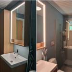 Badezimmer mit beleuchtetem Spiegel, Waschbecken und Dusche.