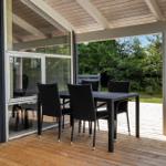 Patio with table and chairs under roof, view of green garden.