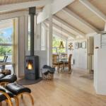 Living area with fireplace, dining area, and kitchen. Wooden floor and large windows.