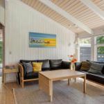 Living room with two leather sofas, wooden table, and wall art. Wooden ceiling and large windows.
