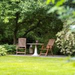 Zwei Holzstühle und ein Tisch stehen auf einer Terrasse im Garten unter Bäumen.