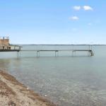 Holzsteg mit Dusche am Strand. Klare See. Himmel mit Wolken.