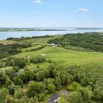 Weitläufige grüne Landschaft mit Wald, Feldern und einem See im Hintergrund.