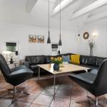 Ein Wohnzimmer mit schwarzem Sofa, drei Stühlen und einem Holztisch.
