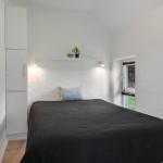Schlafzimmer mit Bett, Schrank und Fenster. Wandregal mit Pflanze und Beleuchtung.