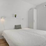 Schlafzimmer mit weißem Bett, Kleiderschränken und Fenster mit Jalousie.