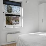Schlafzimmer mit weißem Bett, Kleiderschrank und Fenster mit Blick auf Außenbereich.