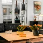 Ein Wohnzimmer mit schwarzer Ledercouch, Holztisch und dekorativen Blumen.