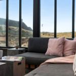 Ein Wohnbereich mit grauem Sofa, rosa Kissen und großem Fensterblick auf Landschaft.