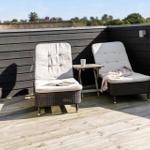 Terrasse mit zwei Liegestühlen, Tisch und Holzboden. Hintergrund: Holzwand und Bäume.