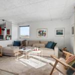 Wohnbereich mit Sofa, Sessel und Küchenzeile. Große Fenster, Wandbilder und rote Schränke.