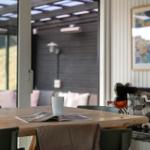 Holztisch mit Tasse und Zeitschrift, Blick auf Terrasse mit Sofa und Wandbildern.