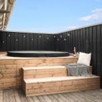 Terrasse mit Holzbank, Sprungmatte und Lichterkette an schwarzer Umzäunung.
