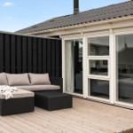 Terrasse mit Sitzgruppe und Blick ins Haus. Holzdeck und schwarze Wand.