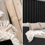 Außenliegende Sofa mit Kissen und Decke auf Terrasse vor schwarzer Holzwand.