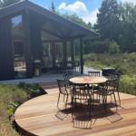 Moderne Holzhütte mit Terrasse, runder Tisch und Stühlen im Grünen.
