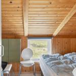 Schlafzimmer mit Holzwand, Bett, Stuhl und Fenster mit Blick auf Grasland.
