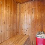 Sauna mit Holzwand und Sitzbank. Holzkiste mit Steinen steht rechts.