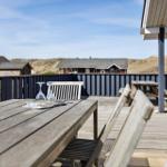 Terrasse mit Holztisch und Stühlen, Blick auf Strandhäuser und Dünen.