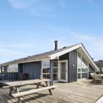 Moderne Villa mit großem Holzdeck, Picknicktisch und Liegestühlen unter blauem Himmel.