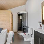 Badezimmer mit Dusche, Toilette und Waschbecken. Holzdecke und -wände.