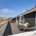 Terrasse mit Liegen und Tisch. Schwarzes Haus mit weißem Geländer. Blick auf Dünen und Himmel.
