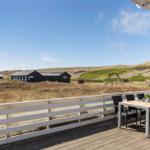 Terrasse mit Tisch und Stühlen. Blick auf Dünensand und Häuser.