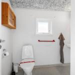 Badezimmer mit Toilette, Fenster, Handtuch und Holzschränkchen an der Wand.