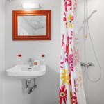 Badezimmer mit Waschbecken, Spiegel und Dusche mit buntem Vorhang.