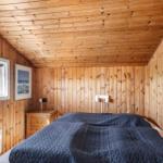 Schlafzimmer mit Holzwand, Bett und Fenster. Wandbild und Nachttisch sichtbar.