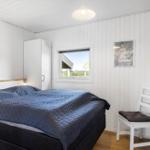 Schlafzimmer mit Bett, Kleiderschrank und Fenster. Weiße Wände und Holzboden.