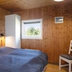 Schlafzimmer mit Holzwänden, Bett, Stuhl und Fenster.
