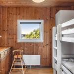 Schlafzimmer mit Doppelstockbett, Holzwand und Fenster mit Blick auf Grün.