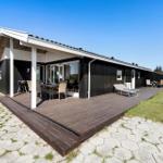 Moderne Villa mit großem Holzterrasse, Grill und Liegen. Blick auf grünen Garten und klaren Himmel.