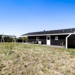 Schwarzes Holzhaus mit Terrasse, Liegestühlen und Schaukel im Gras.