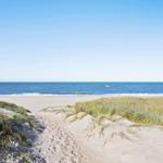 Wanderweg durch Sanddünen zum Strand mit Blick auf das Meer und Windkraftanlagen.