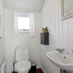 Badezimmer mit Toilette, Waschbecken und Fenster. Weiße Wände und Holzpaneelen.