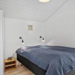 Schlafzimmer mit Bett, Nachttisch und Wandlampen. Wände und Decke sind weiß verkleidet.