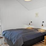 Schlafzimmer mit Bett, Nachttisch und Stuhl. Weiße Wände, Holzboden und Fenster zum Balkon.