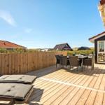 Terrasse mit Liegestühlen und Esstisch. Holzgeländer und Blick auf Häuser.