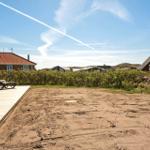 Terrasse mit Liegestühlen und Sandfläche. Hintergrund: Grünhecke und Häuser.
