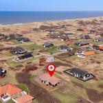 Haus mit rotem Dach in Strandnähe, umgeben von Wiesen und anderen Häusern.