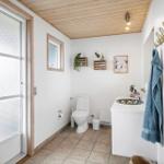 Badezimmer mit Toilette, Waschbecken und Badewanne. Holzdecke und Fenster mit Milchglas.