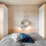 Schlafzimmer mit Bett, Holzwand und weißen Schränken. Wandregal mit Pflanzen und Beleuchtung.