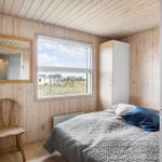 Schlafzimmer mit Holzwand, Bett, Stuhl und Fensterblick auf die Landschaft.