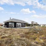 Schwarzes Haus mit Holzterrasse und Schaukel im Grasland unter blauem Himmel.