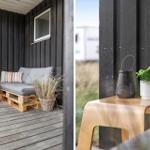 Terrasse mit Sitzbank aus Paletten, Holztisch und Pflanzen vor schwarzem Holzhaus.