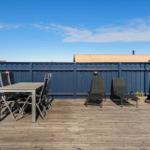 Terrasse mit Tisch, Stühlen und Liegestühlen. Holzdecke und blaue Umzäunung.