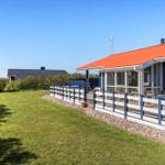 Blau gestrichenes Haus mit rotem Dach und Terrasse. Grasfläche und Zaun im Vordergrund.