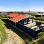 Schwarzes Ferienhaus mit Terrasse und Whirlpool. Roter Dachfirst. Grünflächen und Nachbarhäuser im Hintergrund.